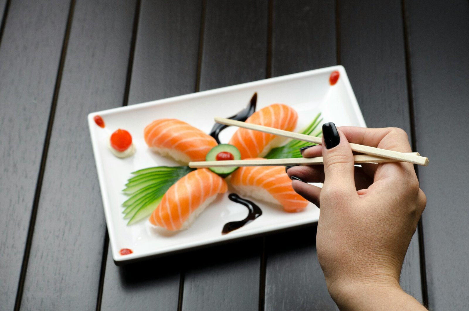 Close-up of a sushi plate with salmon nigiri and decorative garnish, held with chopsticks.